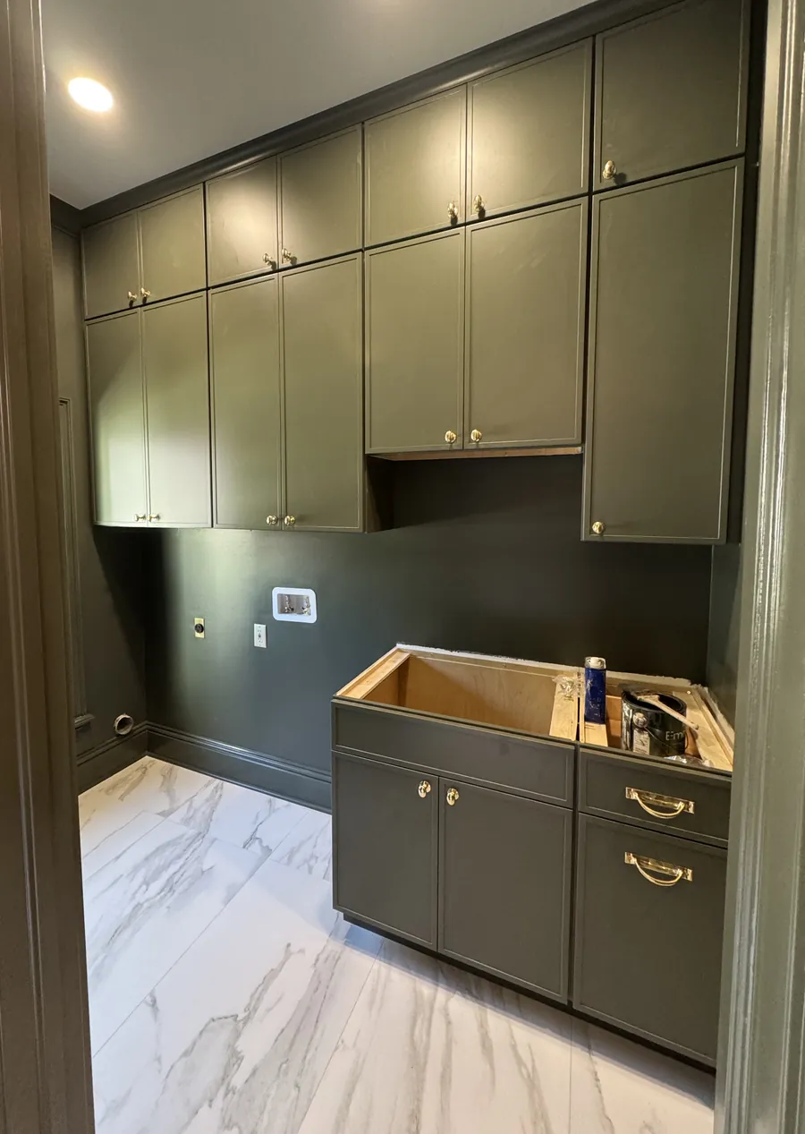Laundry room with green painted cabinets to the ceiling, brass knobs and a marble look floor